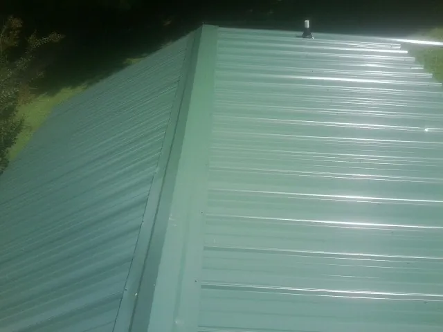 New green metal panels meeting at the ridge of a roof — Flat Roof Repair work by our crew in Canonsburg