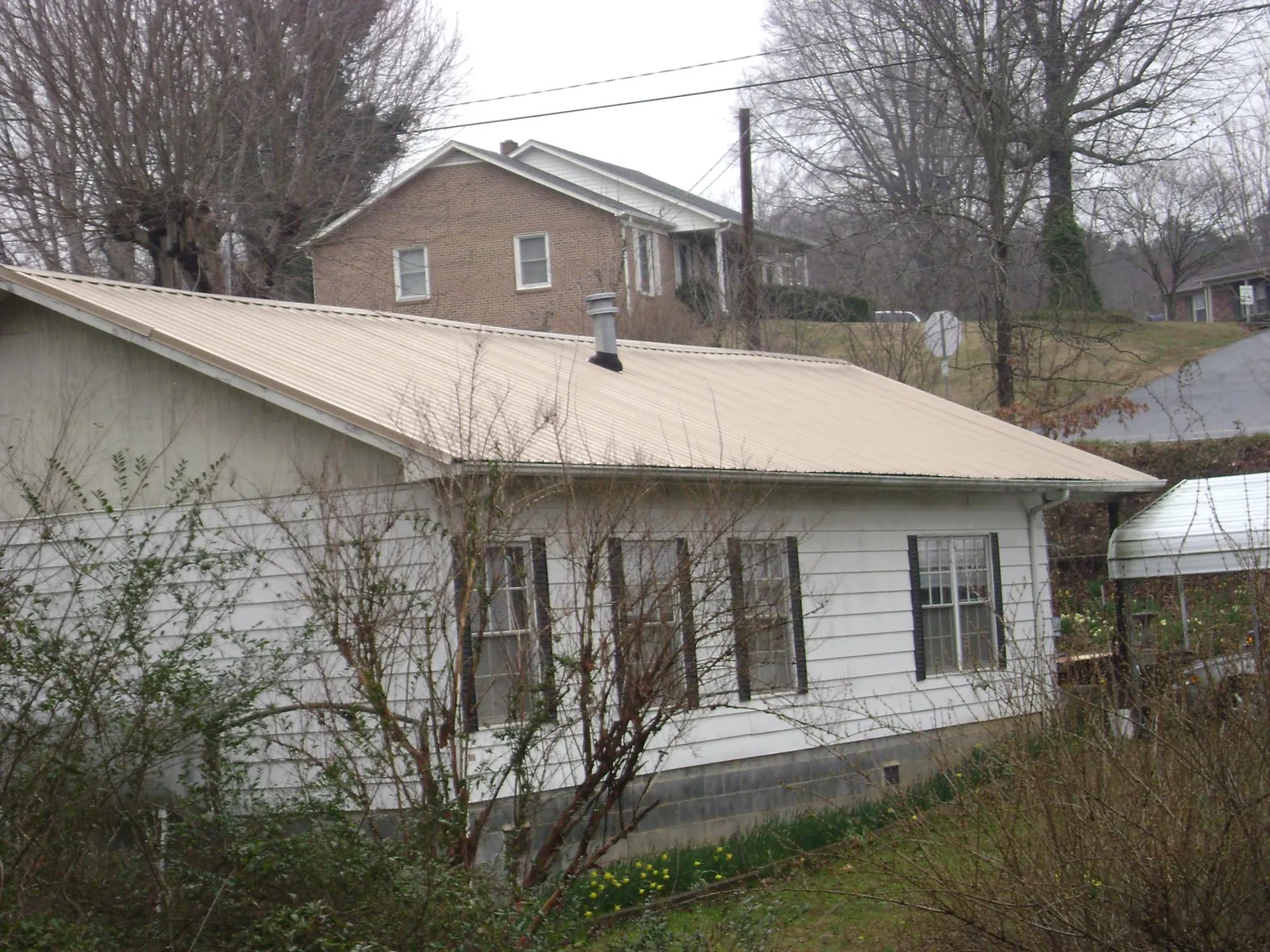 Tan metal roof on a white sided house set into a hillside — Commercial Roofing by Roofing Brothers in Canonsburg